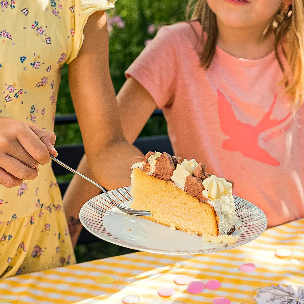 ein Stück Schäfchen-Torte von Oma Barbara von Kuchentratsch auf einem Teller, den ein Kind in der Hand hält