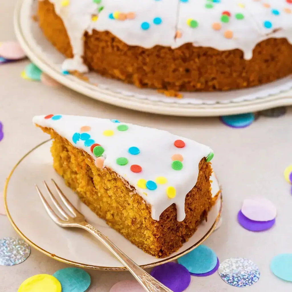 ein Stück Konfetti-Karottenkuchen für Kinder von Oma Irmgard von Kuchentratsch auf einem Teller und Tisch mit Geburtstagsdeko