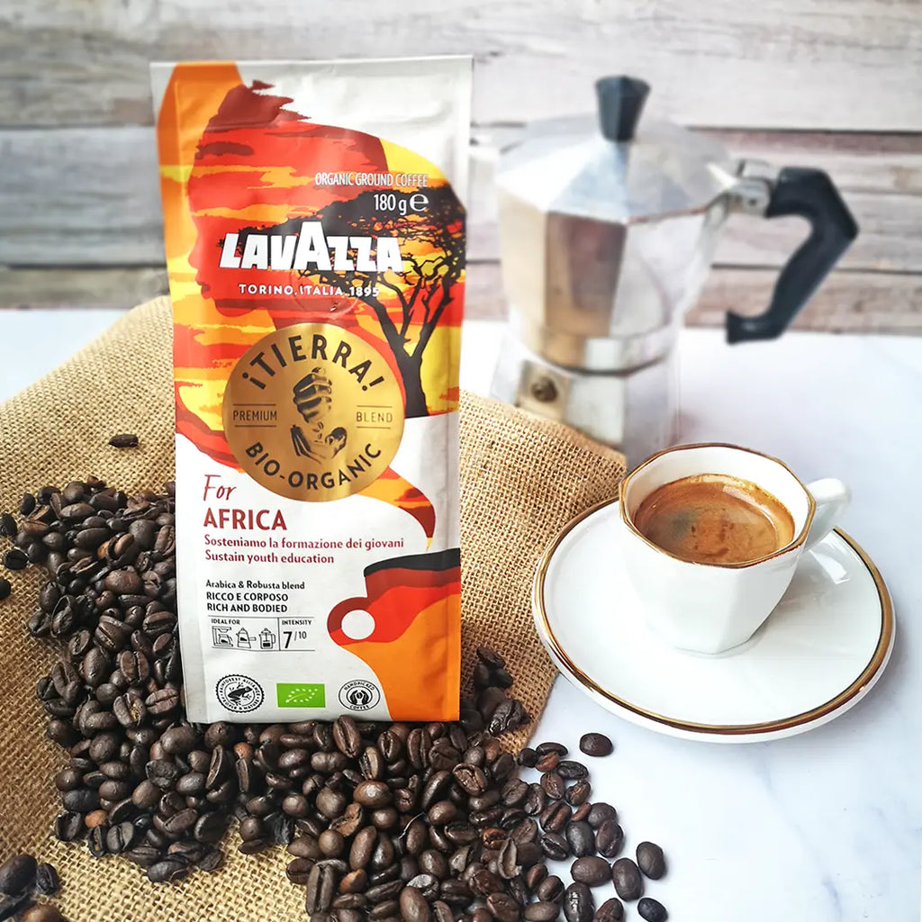eine Packung Lavazza Kaffee „iTierra for Africa“ auf einem Tisch mit einer Mokkakanne, Espresso-Tasse und Kaffebohnen